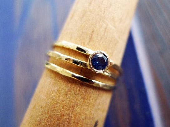 asymmetrical sapphire setting in cup bezel on a wrap ring made of hammered thin bands soldered together. round brilliant cut deep blue sapphire gemstone fair trade. split ring 3 lines 14 karat recycled gold handmade.